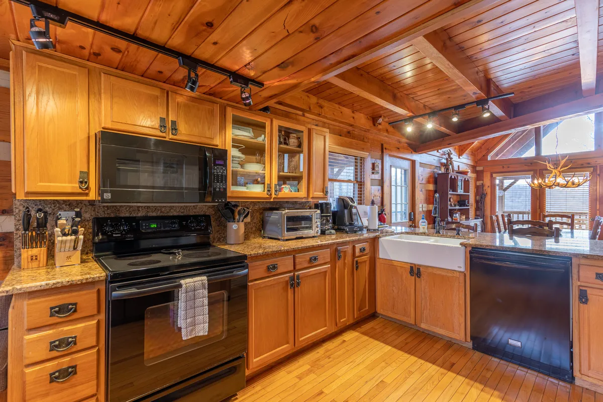 A well-appointed kitchen featuring wooden cabinetry, granite countertops, a farmhouse sink, modern appliances, and a partial view of the dining area beyond. The setting is warm and welcoming, inviting guests to cook, bake, and socialize.