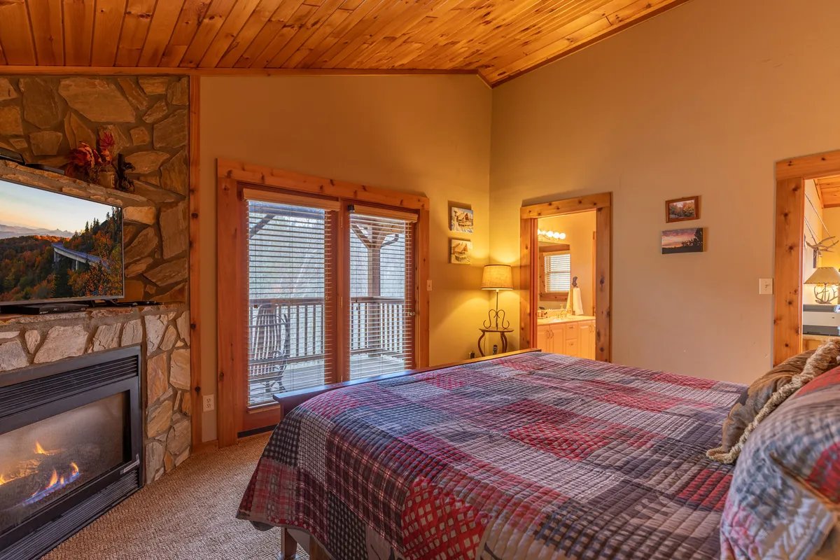 A cozy bedroom anchored by a fireplace, with a comfortable bed and windows that offer views of the surroundings. The warm ambiance invites relaxation, especially after a day of outdoor adventures in any season.