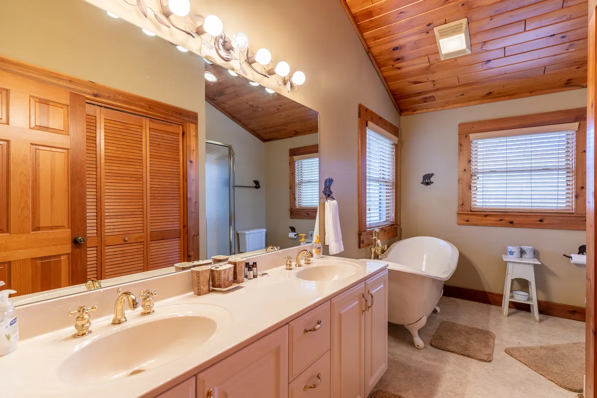 A luxurious bathroom showcasing a double sink with elegant gold fixtures, a freestanding bathtub under a wooden ceiling, and a serene, calming mood. The layout hints at privacy and upscale amenities.