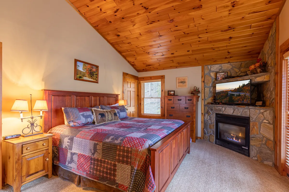 A warm and inviting bedroom featuring a plush bed, a cozy fireplace on one side, a dresser, and tasteful artwork on the wall. The soft lighting and welcoming decor convey a sense of relaxation and personal retreat.