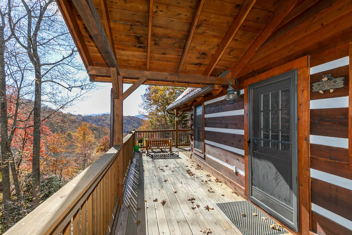 A peaceful wooden deck attached to a charming log cabin, surrounded by trees and offering a panoramic mountain view—ideal for relaxing, gathering, or launching into outdoor activities.